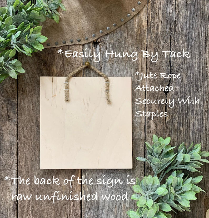 May include: Square wooden sign with jute rope hanger. The sign is light-colored with visible wood grain. Text on the sign reads, "Easily Hung By Tack," "Jute Rope Attached Securely with Staples," and "The back of the sign is raw unfinished wood."