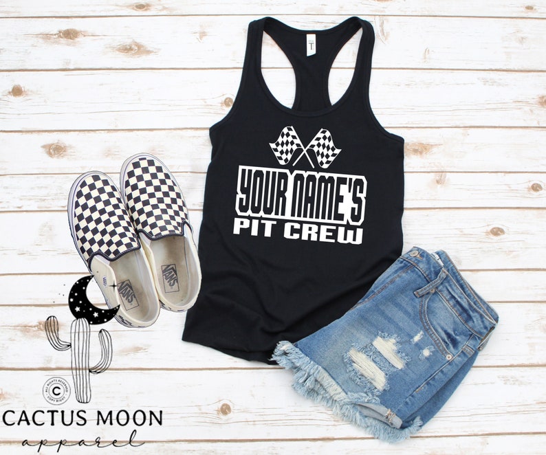 May include: Black racerback tank top with a white checkered flag graphic and the text "YOUR NAME'S PIT CREW". The tank top is paired with denim shorts and checkered Vans shoes.