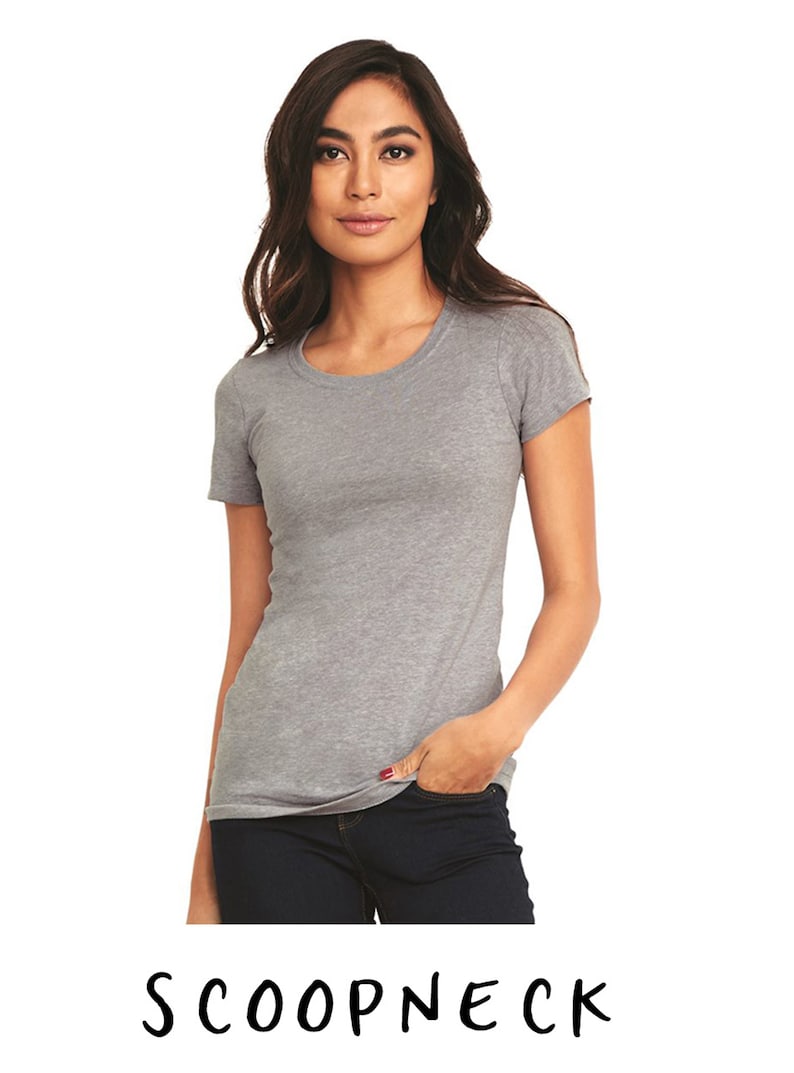 May include: A heather gray scoop neck t-shirt with short sleeves. The model is wearing the shirt with blue jeans.