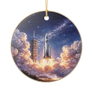 Könnte beinhalten: Runder Keramik-Weihnachtsschmuck mit einer Szene eines Space Shuttle-Starts vor einem sternenklaren Nachthimmel. Das Bild zeigt eine Rakete beim Start, umgeben von Wolken und einem Startturm. Ein goldener Faden ist zum Aufhängen befestigt.