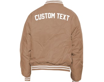 May include: A brown bomber jacket with white ribbed trim around the collar, cuffs, and hem. The back of the jacket has "CUSTOM TEXT" printed in white.
