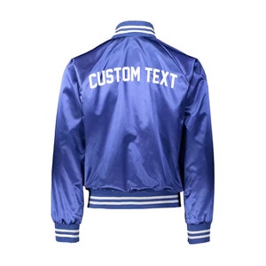 May include: A blue satin bomber jacket with white ribbed trim and the text "CUSTOM TEXT" on the back.