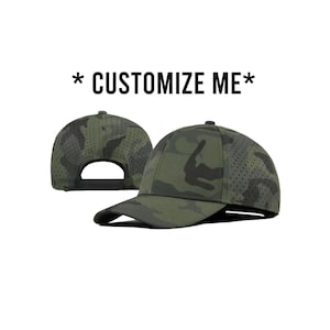 Puede incluir: Una gorra de béisbol de camuflaje verde con un panel de malla. La gorra tiene una correa ajustable negra y una visera negra. El texto "* CUSTOMIZE ME *" está impreso sobre la gorra.