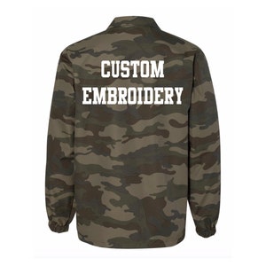 May include: A green and brown camouflage jacket with the text "CUSTOM EMBROIDERY" on the back.