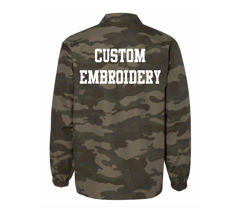 May include: A green and brown camouflage jacket with the text "CUSTOM EMBROIDERY" on the back.
