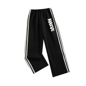 May include: Black athletic pants with white side stripes and the name "MAEVE" printed in white on the side. The pants have a wide leg design and an elastic waistband.