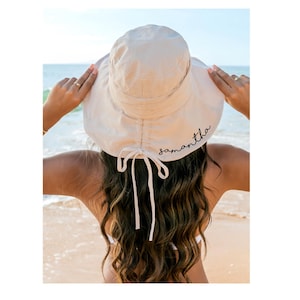 Op de afbeelding: Een beige bucket hat met de naam "samantha" in zwart geborduurd op de achterkant. De hoed heeft een strik aan de achterkant.