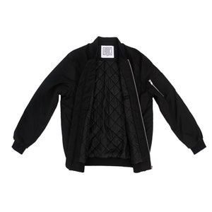 May include: A black bomber jacket with a zipper closure and a quilted lining. The jacket has a pocket on the left sleeve and a label that says "ADOC" on the inside.