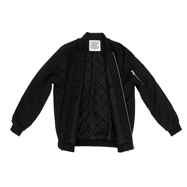 May include: A black bomber jacket with a zipper closure and a quilted lining. The jacket has a pocket on the left sleeve and a label that says "ADOC" on the inside.