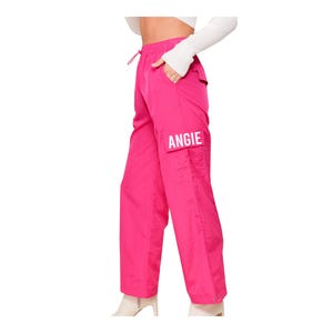 May include: Pink cargo trousers with a white logo that says "ANGIE" on the left leg.