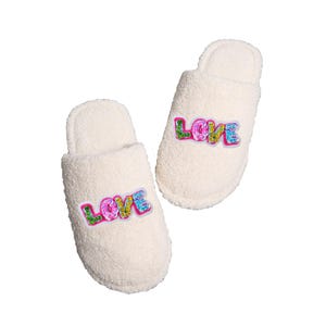 May include: A pair of white fuzzy slippers with the word "LOVE" in colorful, glittery letters on each slipper.