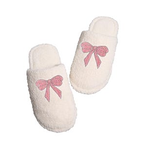 Könnte beinhalten: Ein Paar weiße flauschige Hausschuhe mit rosa Schleifen. Die Schleifen sind aus glitzerndem Material.