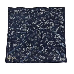May include: A square, navy blue scarf with a white pasta-themed pattern. The design features various pasta shapes, including penne, fusilli, and farfalle. The scarf has the signature "Angie" in gold script in the lower left corner.