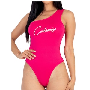 May include: A bright pink one-shoulder bodysuit with the word "Customize" written in white cursive on the front.