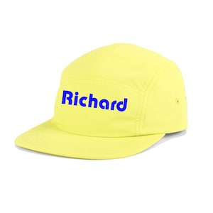 Puede incluir: Una gorra amarilla de 5 paneles con un logotipo bordado en azul que dice "Richard".