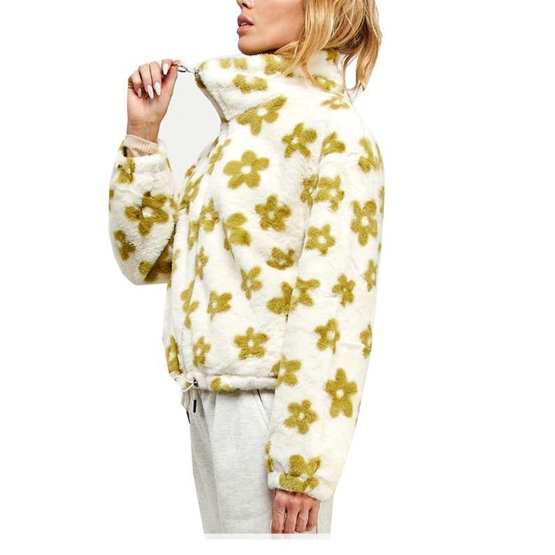 Op de afbeelding: Witte, pluche jas met een groen bloemenpatroon. De jas heeft een hoge kraag en een ritssluiting.