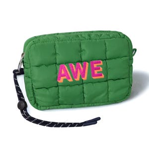 May include: Green quilted pouch with the word "AWE" in pink and orange lettering. The pouch has a black and white wrist strap and a silver zipper. The bag is rectangular and has a puffy, padded appearance.