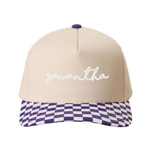 May include: A beige baseball cap with the name "Samantha" embroidered in white script. The brim features a purple and white checkered pattern, and the cap has a purple button on top.