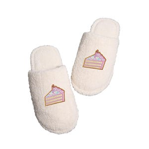 May include: A pair of white fuzzy slippers with a pink and white cake design embroidered on each slipper.