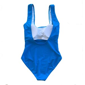 May include: A bright blue swimsuit with a scoop neck and a white lining. The swimsuit has a racerback style.