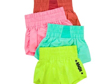 Op de afbeelding: Vier paar sport shorts in verschillende kleuren. De shorts zijn gemaakt van een lichtgewicht, ademende stof. Het bovenste paar is rood, het tweede paar is roze, het derde paar is turquoise en het onderste paar is felgroen. De groene shorts hebben het woord "ANGIE" in het zwart aan de zijkant gedrukt.
