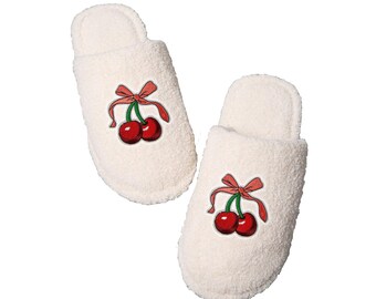 Può includere: Un paio di pantofole bianche e soffici con un design di ciliegie rosse e steli verdi. Le ciliegie hanno un fiocco rosa sullo stelo.