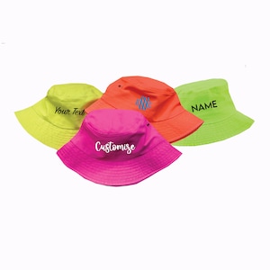 May include: Four neon colored bucket hats with different embroidery. The hats are yellow, pink, orange, and green. The embroidery includes the words "Your Text", "Customize", "NAME", and a monogram.