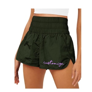 May include: Dark green athletic shorts with a high elastic waistband and a side slit. The shorts have the word "customize" embroidered in purple on the right leg.