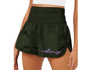 Puede incluir: Shorts deportivos de color verde oscuro con cintura elástica alta y una abertura lateral. Los shorts tienen la palabra "personalizar" bordada en morado en la pierna derecha.