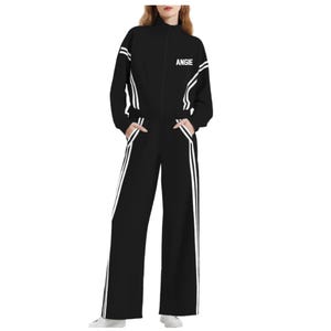 Pode incluir: Fato de treino preto com riscas brancas e o nome "ANGIE" em texto branco. O casaco tem gola alta e fecho de correr. As calças são de perna larga. O fato é feito de um material macio e confortável.