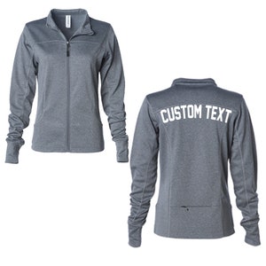 May include: A gray zippered jacket with a stand-up collar and long sleeves. The back of the jacket has "CUSTOM TEXT" printed in white.