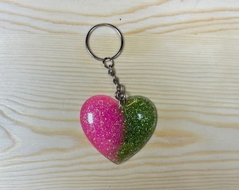 May include: A heart-shaped keychain with a split design. One half is pink with glitter, and the other is green with glitter. The keychain has a silver-colored ring and chain.