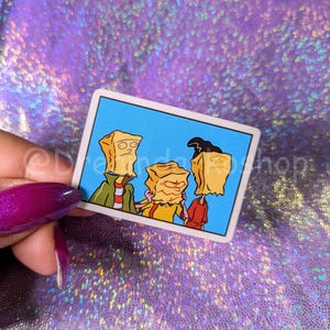 May include: Three cartoon characters wearing brown paper bags over their heads. The characters are standing in front of a blue background. The character on the left is wearing a red and white striped shirt. The character in the middle is wearing a yellow shirt. The character on the right is wearing a red shirt.
