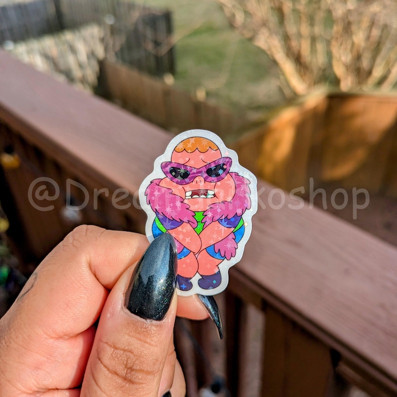 May include: A sticker featuring a cartoon character with pink fur, wearing sunglasses and a green and purple outfit. The character has a surprised expression.