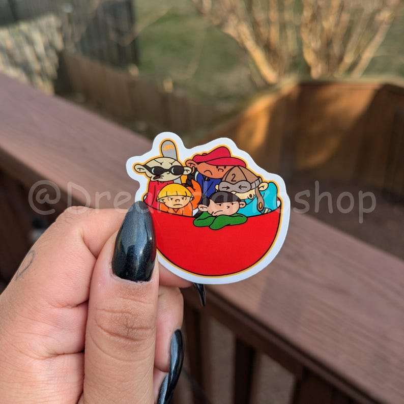 May include: A red bowl sticker featuring five cartoon characters. The characters are wearing different coloured clothing and hats. The sticker is on a wooden surface.
