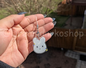 May include: A white bunny charm with yellow and blue stars on a clear acrylic background. The charm is attached to a silver chain.