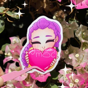 May include: A sticker featuring a cartoon character with purple hair holding a pink heart. The sticker has the text "glazed moc" and is surrounded by pink flowers and white sparkles.