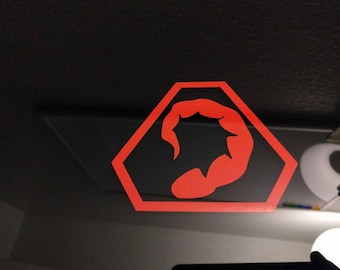 May include: A red scorpion logo sticker in a hexagonal shape on a black background.