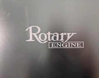 May include: A white sticker on a silver surface with the text "Rotary Engine" in a stylized font.