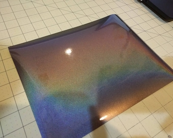 May include: A sheet of iridescent vinyl with a dark brown, blue, and green color shift. The vinyl has a smooth, glossy finish.