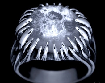 May include: A silver ring featuring a large, round, white stone set in the centre. The stone has a textured surface resembling the moon. The ring band is thick and has a textured design.