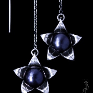 May include: A pair of silver dangle earrings with a black pearl and a star-shaped design.
