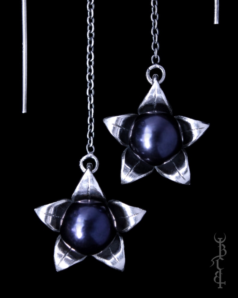 May include: A pair of silver dangle earrings with a black pearl and a star-shaped design.
