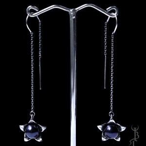 May include: A pair of silver dangle earrings with black pearl accents. Each earring features a delicate flower design with a single black pearl in the center.