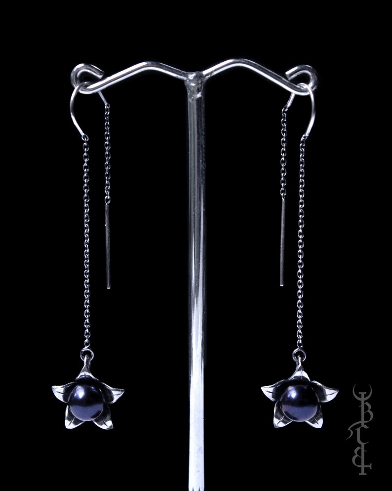 May include: A pair of silver dangle earrings with black pearl accents. Each earring features a delicate flower design with a single black pearl in the center.