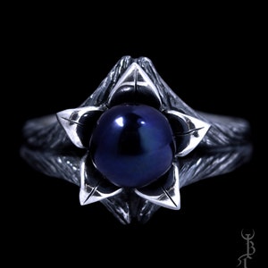 Op de afbeelding: Een zilveren ring met een donkerblauwe parel in een bloemvormig ontwerp.