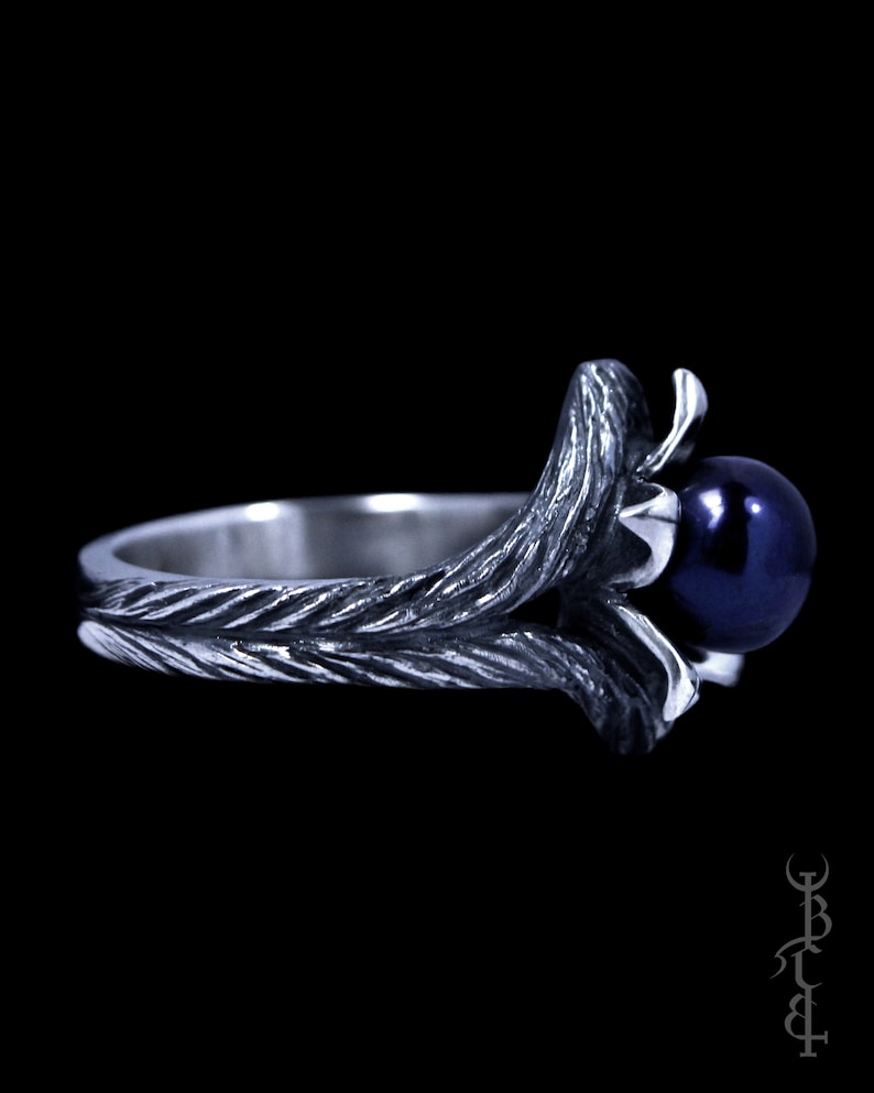 Op de afbeelding: Een zilveren ring met een donkerblauwe parel gezet in een gedraaid takontwerp.
