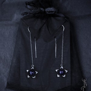 May include: A pair of silver star-shaped earrings with dark purple beads hanging from a black velvet bag.