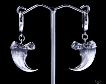 May include: A pair of silver claw earrings with a detailed design. The earrings are hanging from a silver hoop.
