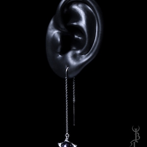 May include: A silver dangle earring with a black pearl and a star-shaped design. The earring is hanging from a black chain.